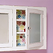 Ausschnitt eines Wandschränkchens mit offener Tür und geblümter Innenwand