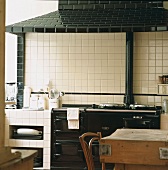 Weiß gekachelte Küche mit antikem, schwarzen Herd und schwarz gekacheltem Dunstabzug