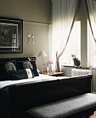 Pearl grey bedroom with black double bed, scatter cushions with Roman emperor motifs and cat on windowsill