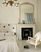 Ruhiges Schlazimmer mit prunkvoll gerahmtem Spiegel über dem Kamin, einem Bett-Kopfende mit schlichtem Blumenmuster und einem Kristallkronleuchter