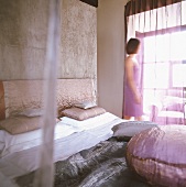 Woman in bedroom looking through purple chiffon curtain