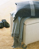 Woollen cushion and blanket on ottoman on castors