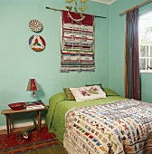 Doppelbett mit bunter Tagesdecke unter Wandteppich