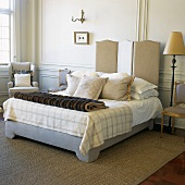 Französisches Bett mit diversen Kissen und Felldecke vor Wandvertäfelung
