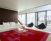 Modernes Wohnzimmer mit schwarzen Designerstühlen, weißer Couch und transparenter Couchtisch auf roten Teppich