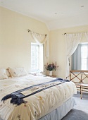 Hohes Doppelbett mit geblümter Bettdecke vor Holzbank unter Sproßenfenster