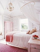 Feminines Schlafzimmer mit Doppelbett unter Moskitonetz und rosa Kleiderschrank an Holzwand