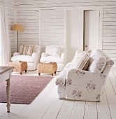 Zwei weiße Sessel und geblümte Couch im maritimen Wohnzimmer mit weiß lackierten Dielenwänden