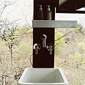Waschbecken und Armaturen in einer Holzsäule vor Panoramafenster mit Blick auf den Wald