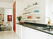 weiße Küche mit schwarzer Arbeitsfläche und rotem Wandschrank vor Esszimmer mit Holztisch