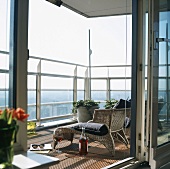 Offene Weinflasche und Weinglas neben Sonnenliege auf Dielenboden eines Balkons mit Aussicht auf die Skyline