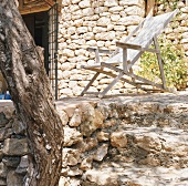 Holzliegestuhl auf Terrasse vor Steinfassade mit Treppenstufen