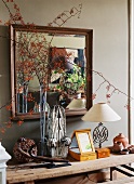 Wandausschnitt mit quadratischem Spiegel mit Holzrahmen; darunter eine rustikale, dekorierte Ablage