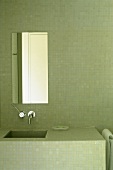 Ausschnitt eines mit grünen Mosaikfliesen rundum gefliestes Badezimmer mit gemauertem Waschtisch und schmalem Spiegel