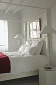 Helles, freundliches Schlafzimmer in Weiß mit Holzwänden und einem zentralen Doppelbett
