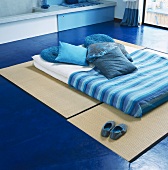 Futon with blue scatter cushions & blue blanket on tatami mats on floor
