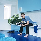 Man sitting on bench against wall reading in blue interior