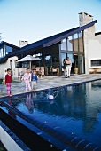 Parents watching children playing with ball in pool with house in background