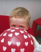 Kleiner Junge bläst Luftballon mit Herzen auf