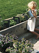 Kleines Mädchen giesst Kräutergarten