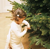 Kleines Mädchen mit Engelsflügel schmückt Weihnachtsbaum