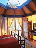 Gemütliches Schlafzimmer aus Holz mit verglastem Kuppeldach und vielen Fenstern
