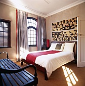 Großes Doppelbett und Holzbank in einem Raum mit hohem Fenster und stuckierter Decke