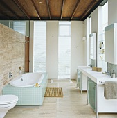 Modernes Badezimmer mit raumhohen Fenstern, teilverglaster Natursteinwand und Holzbalkendecke