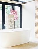 Freistehende Badewanne in einem Raum mit Backsteinwand und großer Terrassentür