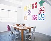 Einfacher Holztisch und weiße Stühle in loftartigem Raum mit bunten Wandbildern