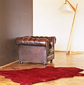 Ein Chesterfield Ledersessel neben einer Stehleuchte aus Holz und ein roter Fellteppich