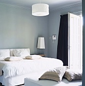 Weisses Bett in einem hellblauen Schlafraum mit Stuckdecke und Terrassentür