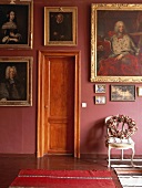 Barocke Portraitgemälde mit prunkvollen Bilderrahmen gruppieren sich um eine klassische Holztür