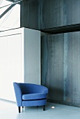 Ein blauer Sessel vor einer grauen Wand mit Einschnitt und einem weissen Einbauschrank