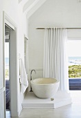 Eine minimalistische Badewanne in einem Badezimmer mit schöner Aussicht über die Terrasse aufs Meer