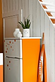 Ein orange bemalter Kühlschrank vor einer alten, weissen Holzwand