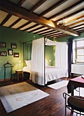 Ein Himmelbett im gemütlichen Schlafzimmer mit uriger Holzbalkendecke und grünen Wänden