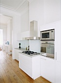 Einbaugeräte aus Edelstahl in einer weissen Designerküche im großzügigen, offenen Wohnraum mit Dielenboden und Stuckdecke