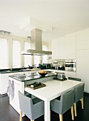 In der weissen Designerküche fügt sich ein minimalistischer Esstisch in den Küchenblock ein