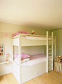 Ein einfaches, weisses Stockbett in einem aufgeräumten Kinderzimmer mit rosa Details