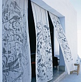 Leicht transparente Stoffstores mit floralen Ornamenten dienen als Sicht- und Sonnenschutz des offenen Wohnraums