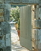 Eine geöffnete Holztür führt auf das Grundstück eines alten Landhauses