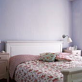 Romantische Schlafzimmereinrichtung in Weiß mit Blumenbettwäsche vor einer fliederfarbenen Wand