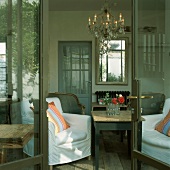 Blick durch die geöffnete Terrassentür in das Wohnzimmer mit Kronleuchter und verschiedenen Sesseln