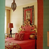 Ein rotes Bett mit prunkvoll verziertem Kopfteil, darüber eine orientalische Hängeleuchte