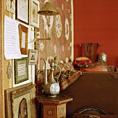 Antike Teekanne auf marokkkanischem Beistelltisch vor einer Bilderwand mit goldener Wandleuchte