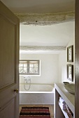 Kalksteinbadewanne im kleinen Badezimmer mit schräger Holzbalkendecke und Dielenboden