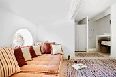 Farbenfrohe Sitzpolster vor einem kleinen Rundfenster und bunte Flickenteppiche im Wohnzimmer mit Holzbalkendecke
