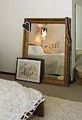 Halsketten an einem Spiegel mit Goldrahmen und eine gerahmte Zeichnung am Boden eines Schlafzimmers