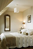 Nackenrollen und Zierkissen auf der Tagesdecke eines Doppelbettes im Schlafzimmer mit Gaubenfenster
